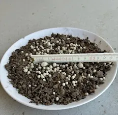 Kalk mit Schwefel, Körnung über 4 mm, auf Erde mit Zollstock zum Größenvergleich